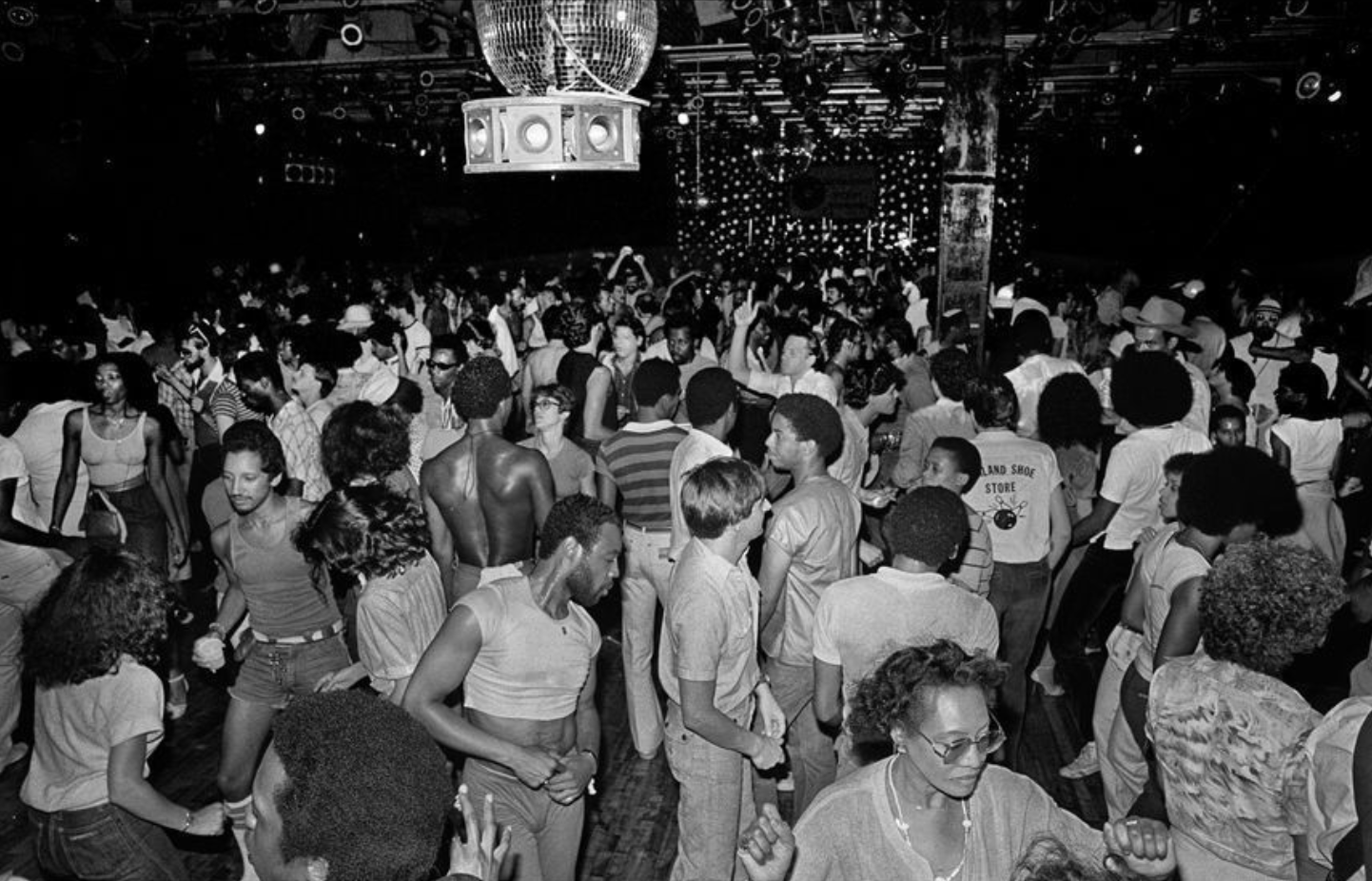 A wide view of a packed nightclub dance floor with a mirror ball overhead.