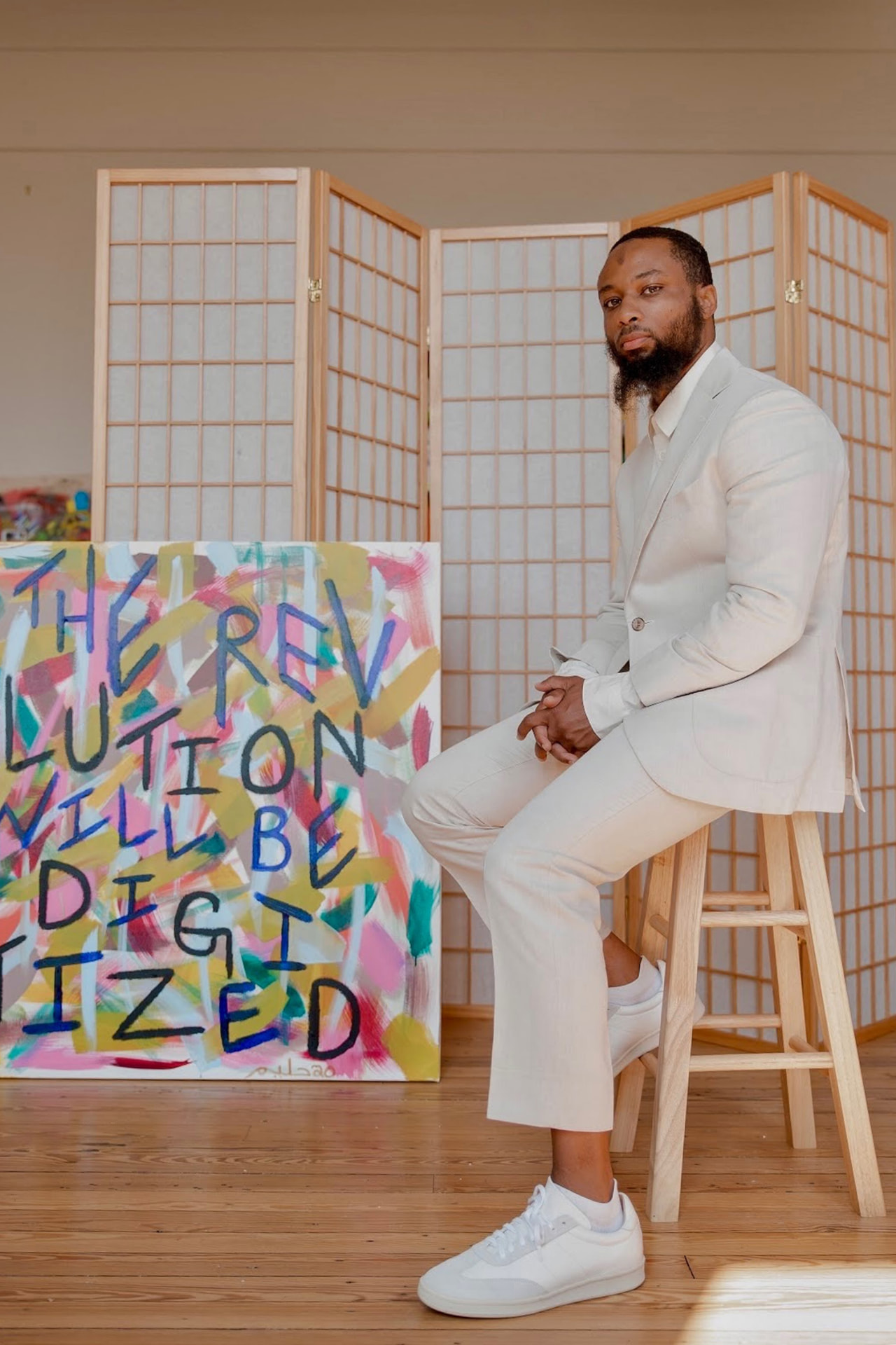 Halim Flowers seated beside a painting that reads The Revolution Will Be Digitized.