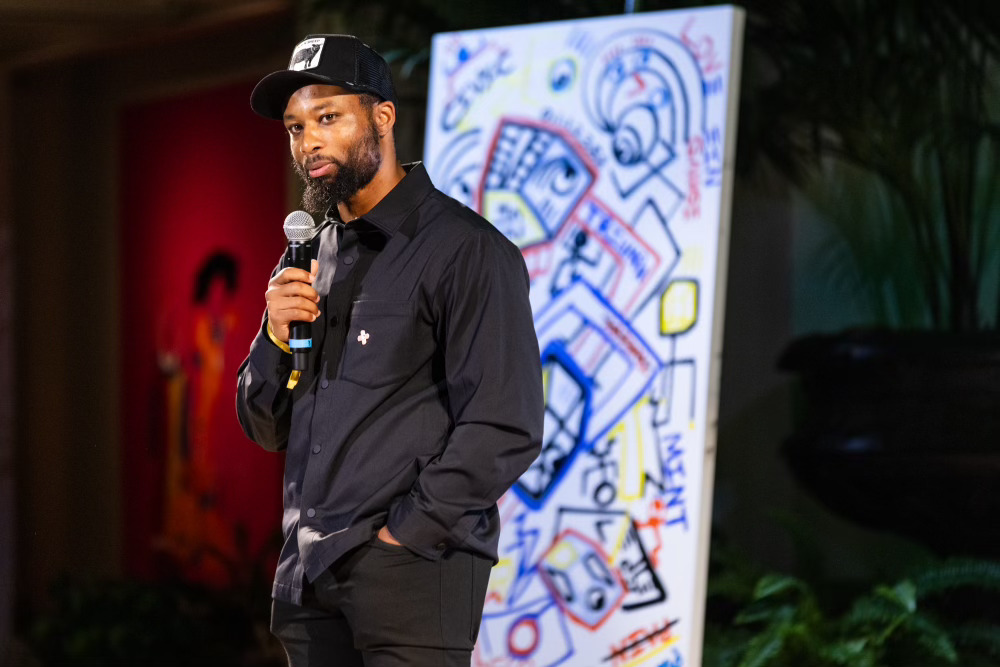 Halim Flowers holding a microphone in front of one of his paintings.